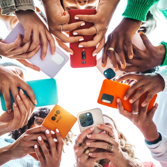 Fotoğrafta, daire şeklinde duran yedi kişi, başlarını eğmiş, göğüs hizasında tuttukları telefonlarla ilgileniyor. Aşağıdan çekilmiş fotoğrafta, ellerinin arasındaki telefonlardan kişilerin yüzleri görünmüyor.